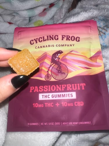 Customer holding a single amber Passionfruit Gummy with the product packaging in the background.