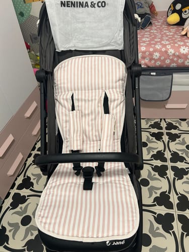 Cliente muestra la colchoneta Evolution Fine line Pink, con rayas rosas y blancas, instalada en una silla de paseo negra.