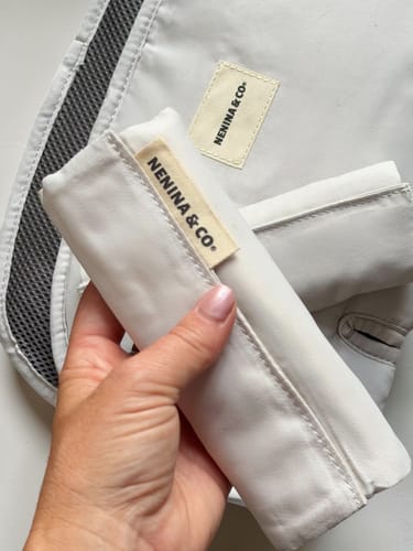 Primer plano de la mano de un cliente sosteniendo uno de los protectores de tirantes beige a juego con la Colchoneta Evolution.
