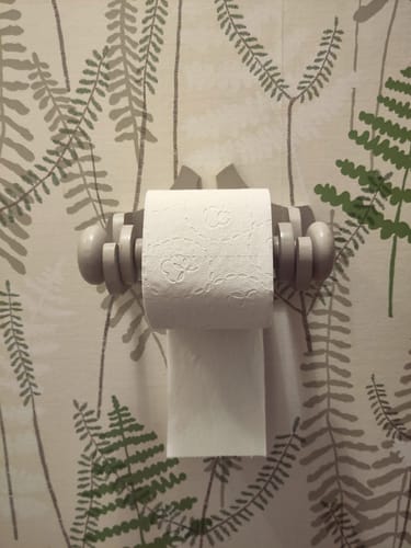 Client montrant le papier toilette triple épaisseur sur un support mural.