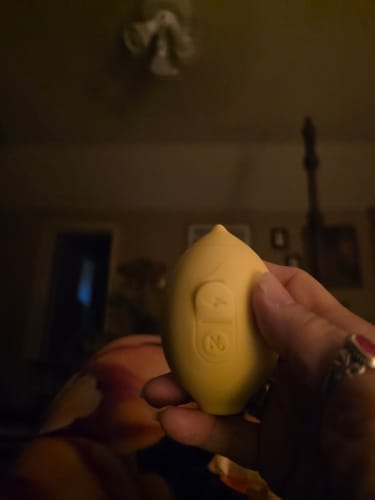 Reviewer holding the yellow Lem Clitoral Massager in a dimly lit room, showing the control buttons.