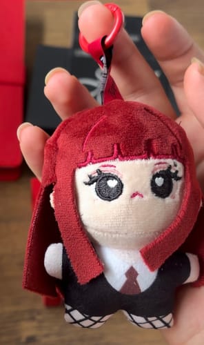 Customer's hand holding the Jennie × Miniso cotton doll plush keychain with red hair and a detailed outfit.