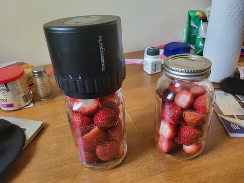 Customer using the black Mason Genie Vacuum Sealer to seal a glass mason jar filled with fresh strawberries.