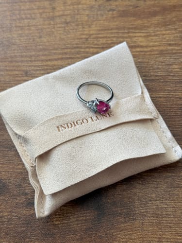 Customer's Leesha Birthstone Ring with a pink and clear stone displayed on its beige pouch.