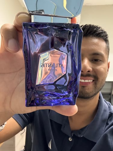 Un cliente sonriente sostiene el frasco azul y geométrico del perfume French Avenue Atlantis.