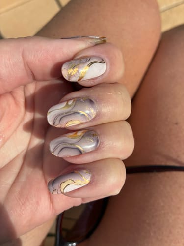 Nahaufnahme der Hand einer Kundin, die ihre manikürten Nägel mit den 'Metallic Marble' Nagelfolien in Marmoroptik zeigt.