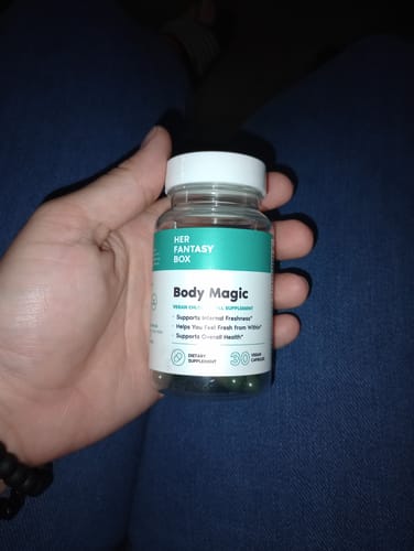 Reviewer's hand holding a clear bottle of Body Magic Chlorophyll Pills, showing the dark green capsules inside.