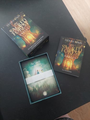 Rezensent zeigt die ausgepackten Sacred Forest Orakelkarten, die offene Box und das Guidebook auf einem Tisch.