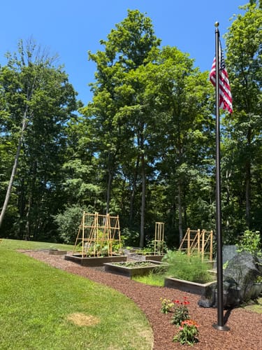 Customer's tall commercial flagpole with an American flag, installed in a landscaped backyard garden.