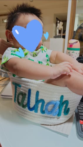 Reviewer's baby sitting inside a personalized knitted basket with the name 'Talhan' in multicolor yarn.