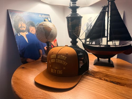 Customer's brown and black Big Tall Trucker Hat sitting on a wooden table.