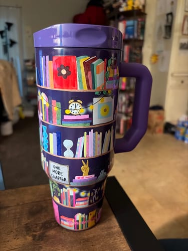 Customer's purple Thicc Buddy mug featuring a colorful bookshelf pattern on a wooden surface.