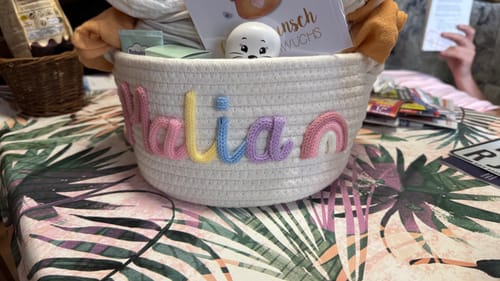 Customer's Baby Knits personalized knitted basket with rainbow icon and the name Malia in colorful yarn letters.