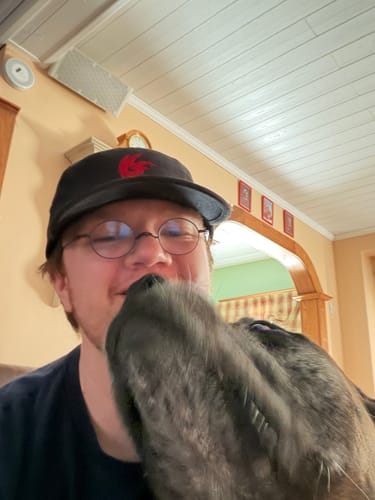 Reviewer's custom embroidery hat with a black cap and red design, worn while a dog nudges them.