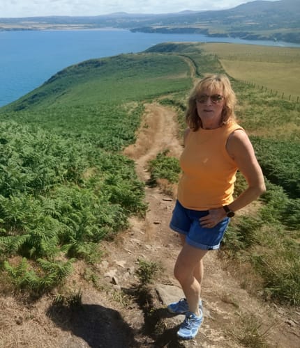 Customer's Active II Pro barefoot shoes worn by a person hiking on a grassy cliff trail by the sea.