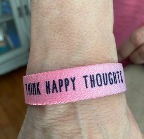 Customer's pink Think Happy Thoughts bracelet worn on a wrist.