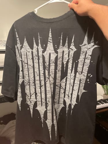 Reviewer's black Revenge Tee held on a hanger, displaying a large grungy white logo on the back.
