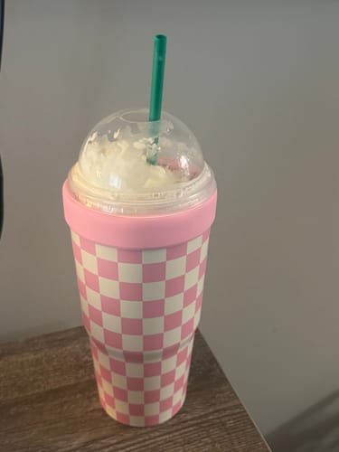 Customer's pink checkered To-Go Buddy cup containing a drink with a clear dome lid and green straw on a wooden surface.