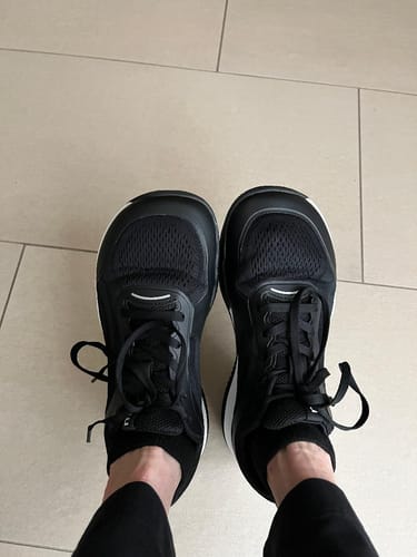 Customer's feet wearing black CUURT Muuv court shoes with wide toe boxes, showing a top-down view.
