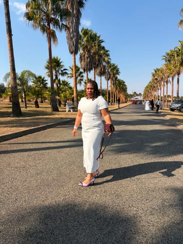 Customer's burgundy SKARLET063 side bag carried by a person wearing a white dress on a palm tree-lined road.