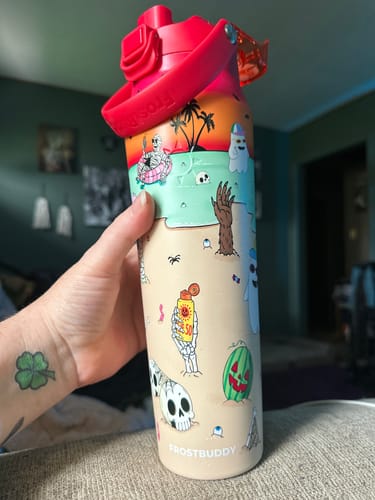 Customer's hand holding a festive Bottle Buddy with a pink lid and colorful Halloween beach-themed print.
