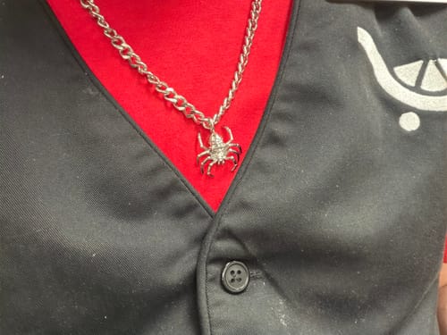 Customer's silver Spider Skull Pendant on a chain, worn over a red and black shirt.