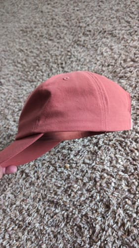 Customer's terracotta red Big Relaxed Cap held by a hand against a textured carpet background.