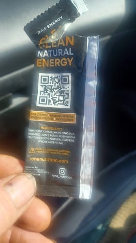 Customer's hand holding a torn packet of SuperCharged Honey showing the ingredients list and a QR code.