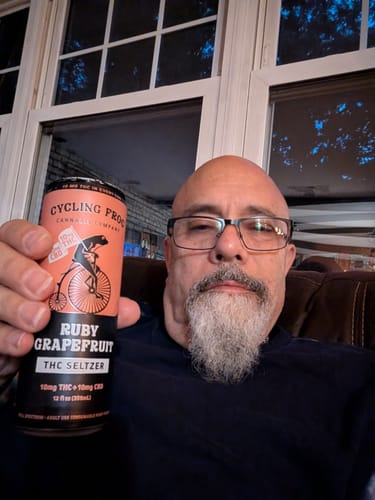 Reviewer holding a can of Cycling Frog Ruby Grapefruit THC Seltzer while relaxing at home.