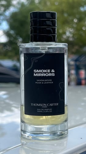 Customer's Smoke & Mirrors Eau de Parfum bottle with clear glass and black label, standing outdoors.