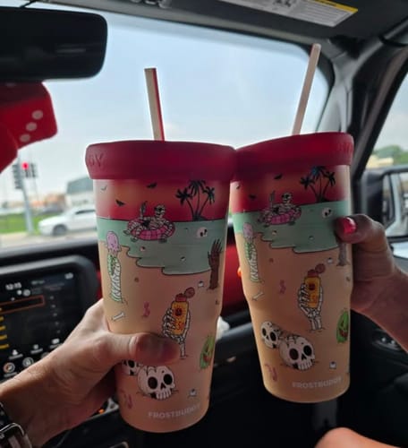 Customer's hands holding two Sunscream To-Go Buddy tumblers with a beach-themed print inside a car.