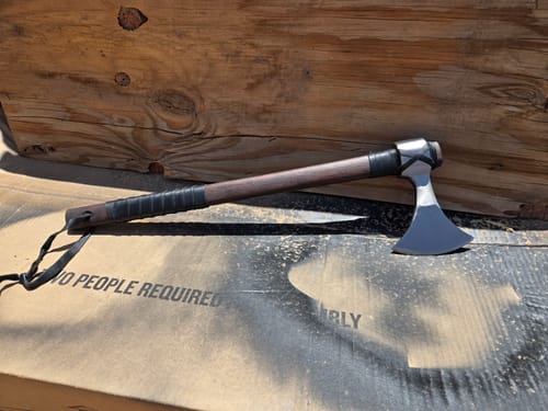 Customer's hand-forged Vindflaug axe with a wooden handle and leather wrap, resting on a flat surface.