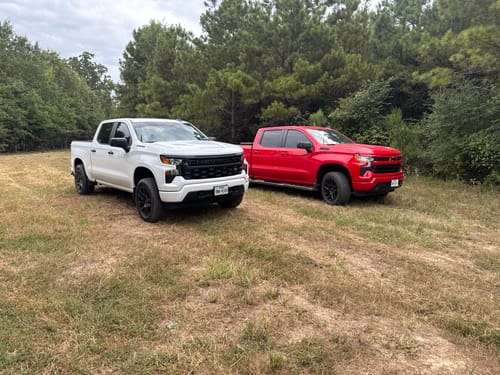 Customer's white and red Chevy Silverado trucks parked in a grassy field after installing Aluminum Upper Control Arms.