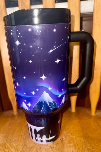 Customer's 50oz Thicc Buddy in Nightfall print showing a mountain and starry night sky scene on a wooden table.