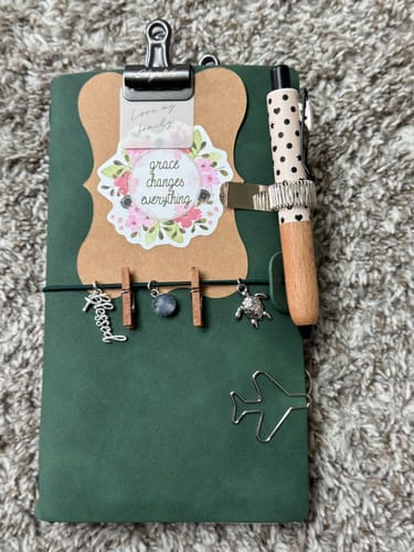 Reviewer's Star & Heart pen with wood-grain grip attached to a green journal decorated with charms and a clip.