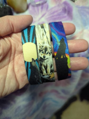 Customer's hand holding three colorful Mystery Club+ bracelets featuring wolf and puppy designs.