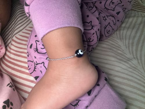 Reviewer's silver Evil Eye Cutie Kids Anklet worn on a baby's ankle with a prominent dark bead.