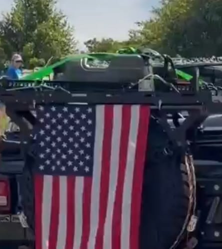 Customer's Tuff Jug 5 Gallon Jug secured with green straps to a vehicle's rear storage rack, partially obscuring a flag.