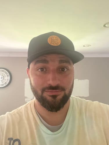 Customer's Big Flat Bill Structured Mesh Hat in black with an orange circular logo, worn by the reviewer.