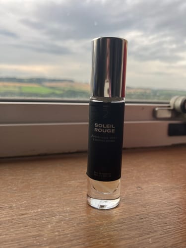 Customer's 10ml travel-sized Soleil Rouge Eau de Parfum bottle standing on a wooden surface against a window.