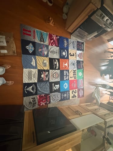 Customer's colorful Project Repat T-Shirt Quilt featuring various graphic prints, spread out on a wooden floor.