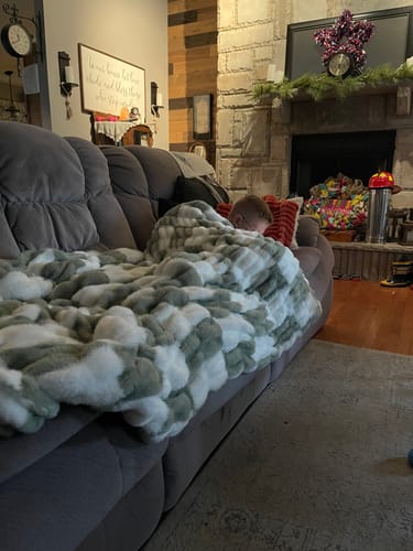 Reviewer's child resting comfortably under a plush sage checkered Hugs Check Sage Blanket on a living room couch.