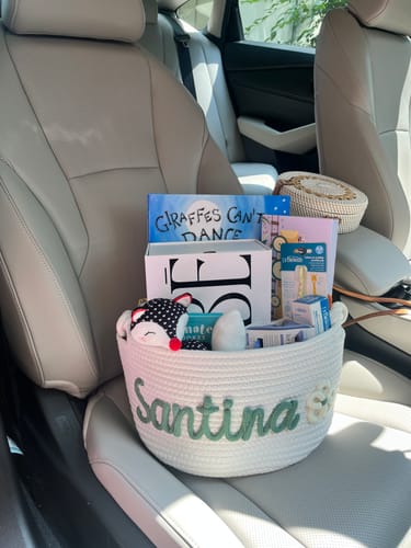 Customer's Baby Knits personalized white cotton basket with sage green name embroidery sitting on a car seat.