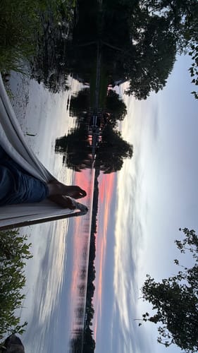 Reviewer's legs resting in The Go Hammock, overlooking a calm lake at sunset.