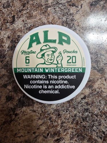 Customer's container of Mountain Wintergreen Nicotine Pouches on a speckled surface.