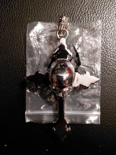Reviewer's shiny silver Down Your Throat pendant shaped like a skull on a cross inside its plastic packaging.