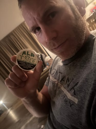 Reviewer holding a round white tin of Mountain Wintergreen Nicotine Pouches in front of their face.