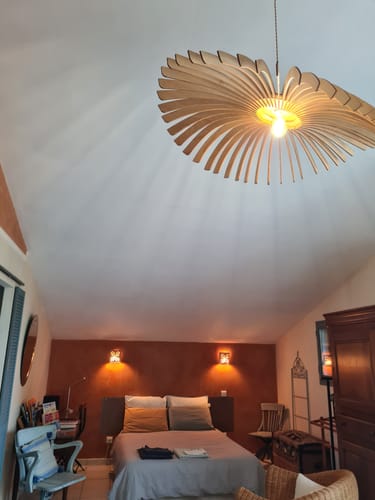 Customer's Ampoule LED E27 12W installed in a large, wooden slatted pendant light fixture in a cozy, warm-lit bedroom.