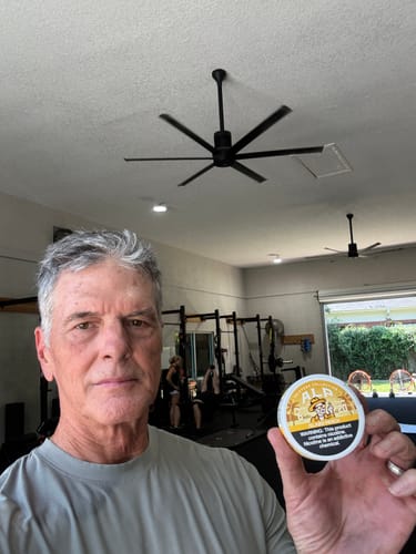 Customer holding a circular, yellow and white can of Drifters Island Peach nicotine pouches in a gym setting.
