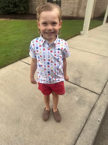 Customer's child wearing the Easy as 123 White Polo with a school-themed print, paired with red shorts.